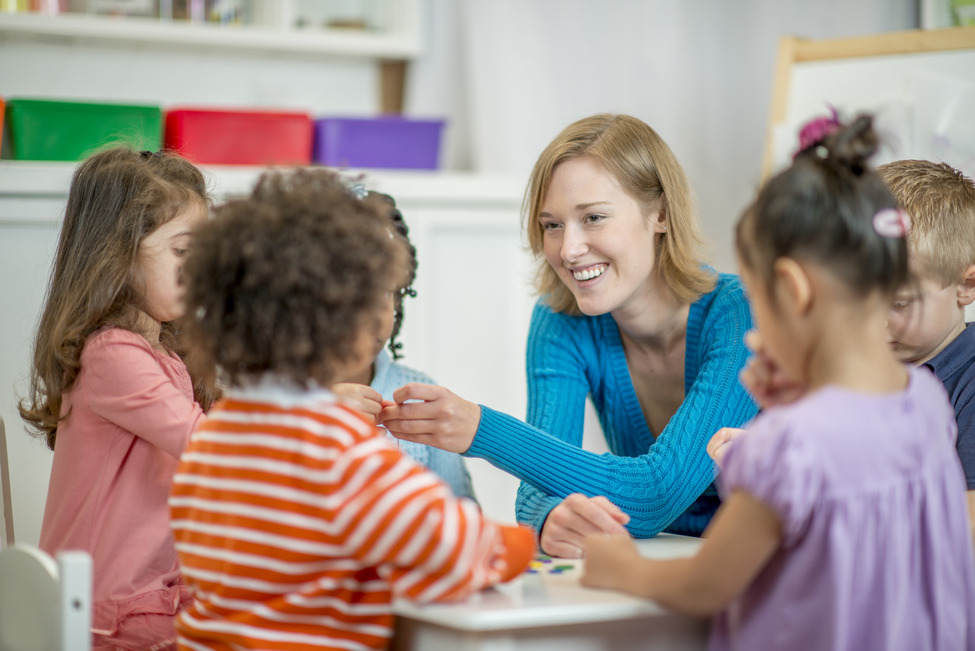 Eine multiethnische Gruppe von Kindern im Grundschulalter sitzt an einem Tisch und reiht Perlen aneinander.